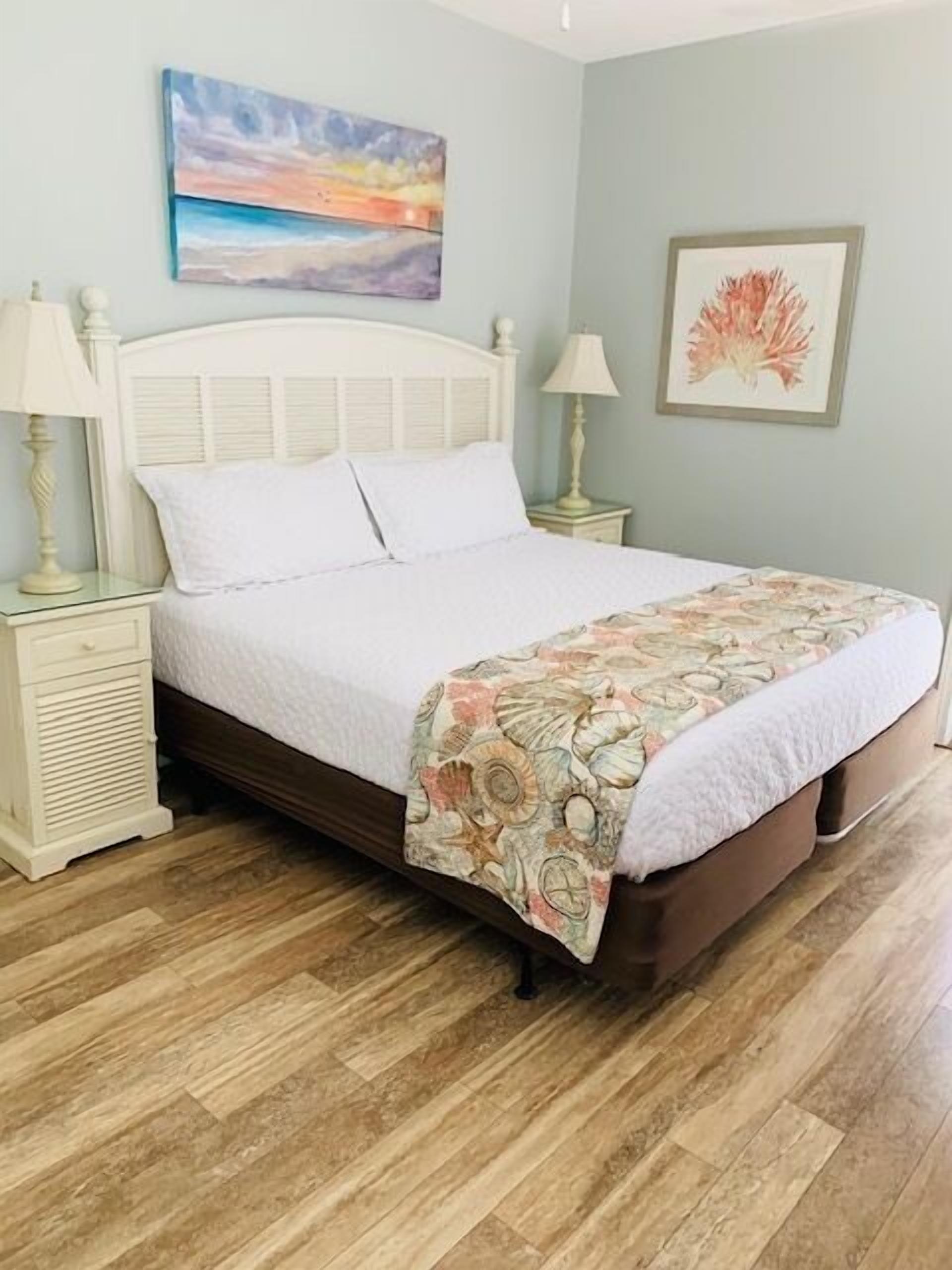 A neatly made bed with a floral bedspread, a white headboard, and two bedside tables with lamps.