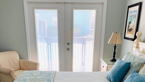 A bedroom with a bed, a chair, a nightstand, and a door with a view to the outside. - Destined for Fun, House, Cabana, Pool + few steps to beach (Destin)