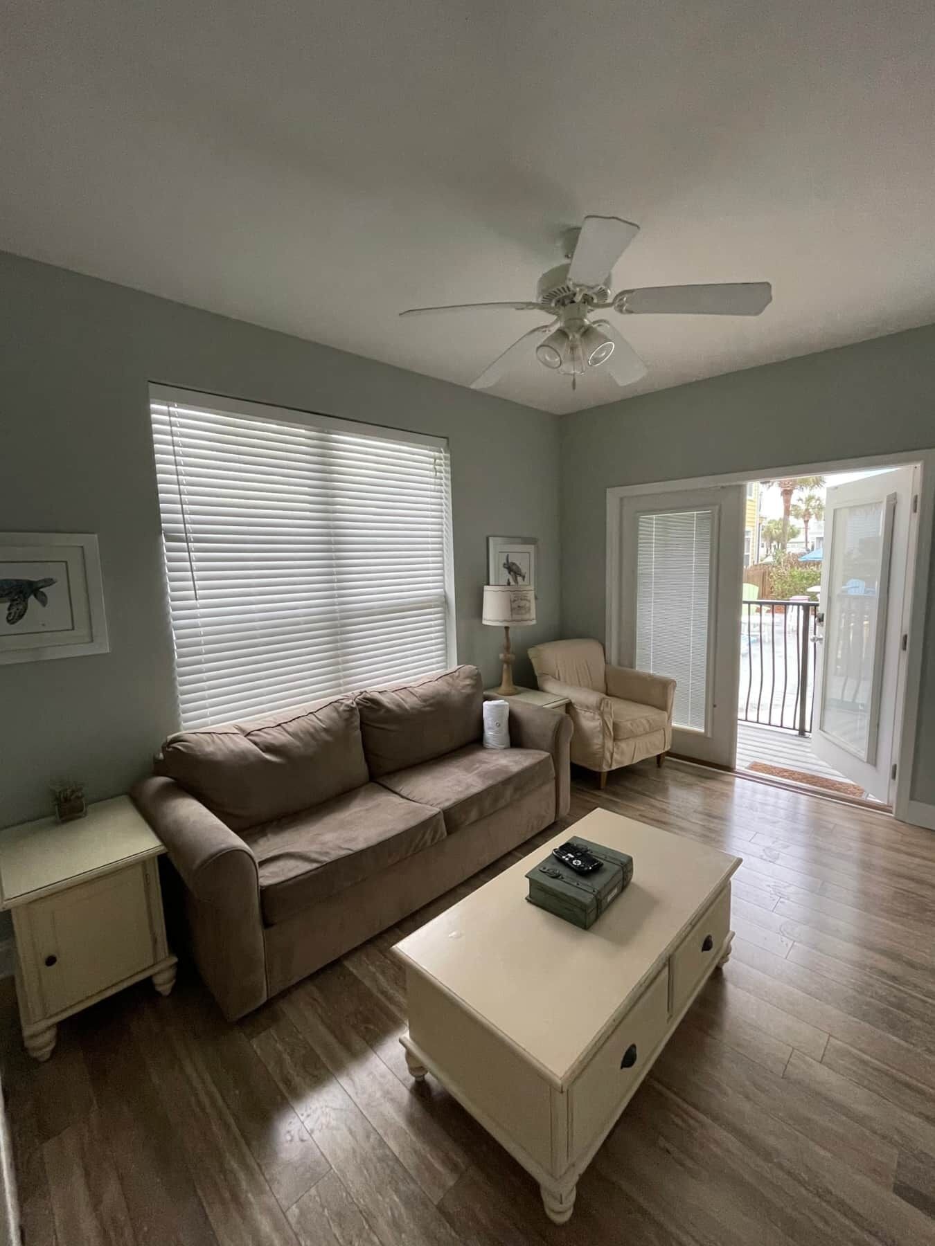 Ein Wohnzimmer mit einem beigefarbenen Sofa, einem weißen Couchtisch, einem Deckenventilator und einer Glastür zum Außenbereich.