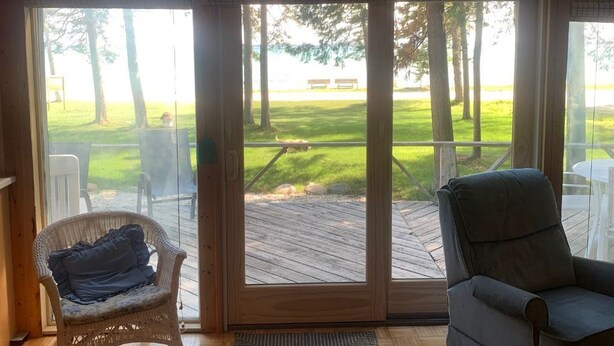 Une pièce dotée d’une grande porte-fenêtre coulissante donnant sur une terrasse, d’un fauteuil en osier, d’un fauteuil rembourré et d’un tapis tissé.