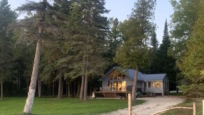 Une maison à deux étages dotée d’un porche couvert, entourée de grands arbres et bordée d’une allée en gravier.