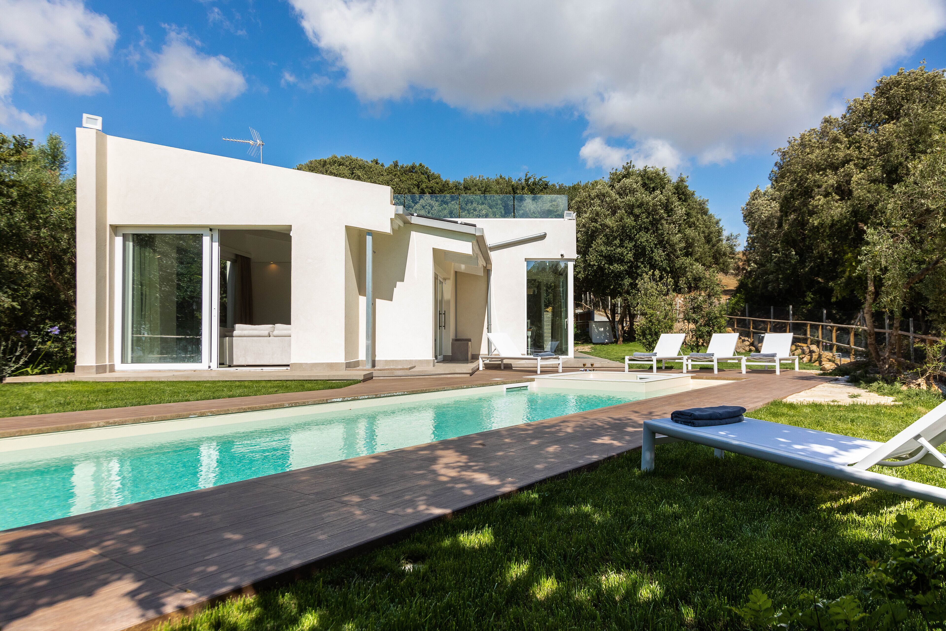 A modern house with a swimming pool, outdoor seating, and a view of the surrounding greenery.