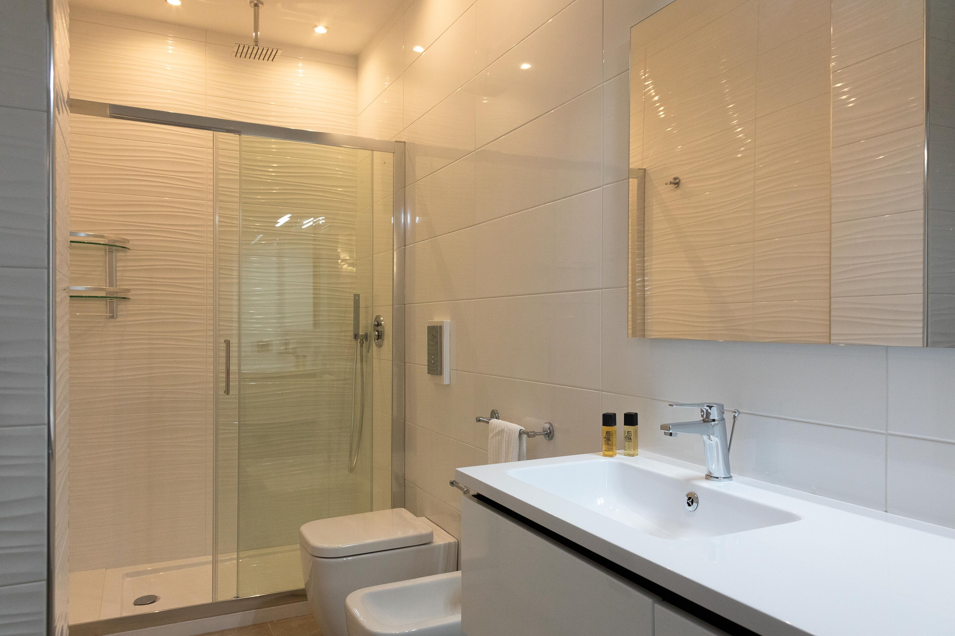 Une salle de bain moderne avec une douche à parois de verre, un lavabo blanc et un grand miroir.