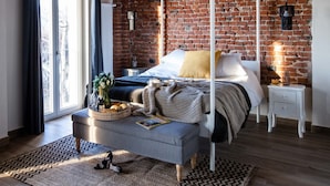 Ein Schlafzimmer mit Himmelbett, Backsteinwand, Holzbalkendecke und großem Fenster mit Vorhängen.