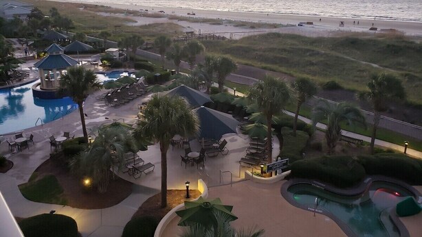 Un resort con múltiples piscinas, zonas de estar al aire libre y vistas a la playa al atardecer.