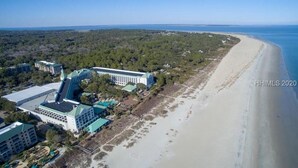 Vista aérea de un hotel frente al mar con varias edificaciones, una playa de arena y una vista despejada del océano.