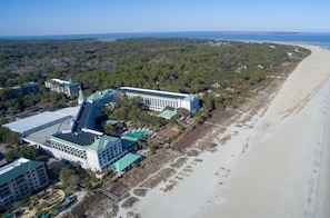 An aerial view of a coastal hotel with multiple buildings, a sandy beach, and a clear view of the ocean.