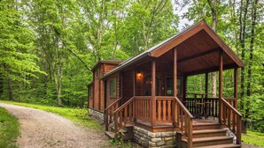 Une cabane en bois dotée d’un porche, entourée d’une forêt.