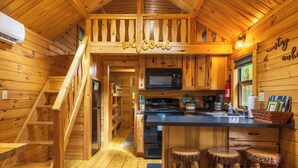 L’intérieur d’un chalet en bois comprend une cuisine, un escalier en bois et une pancarte indiquant « Bienvenue ».