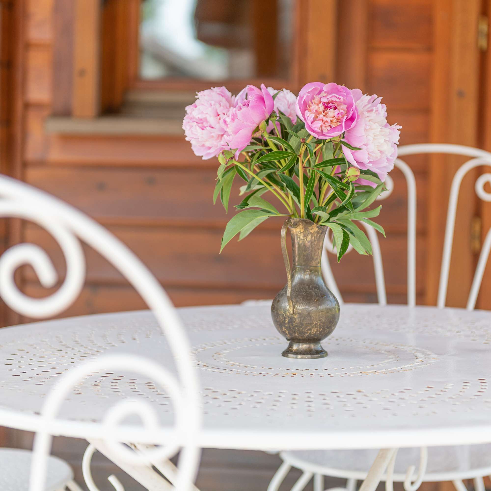 A round white table with a metal vase containing pink flowers.