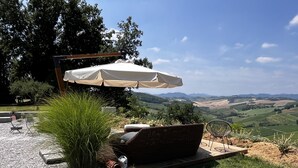 An outdoor seating area with a table and chairs, a large umbrella, and a view of rolling hills.