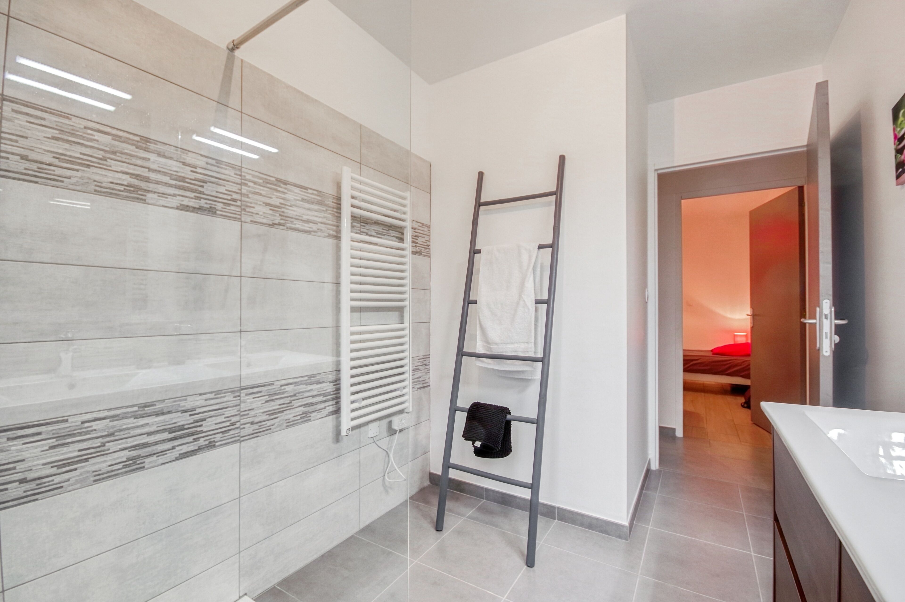 A modern bathroom with a glass shower enclosure, a white towel rack, and a ladder.