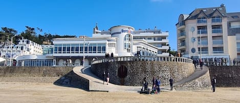 A coastal hotel with a stone retaining wall, a sandy beach, and a clear blue sky.