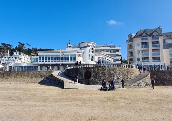 A coastal hotel with a stone retaining wall, a sandy beach, and a clear blue sky.