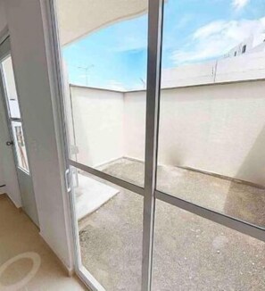 A room with a large sliding glass door leading to a balcony with a concrete floor and a clear sky view.