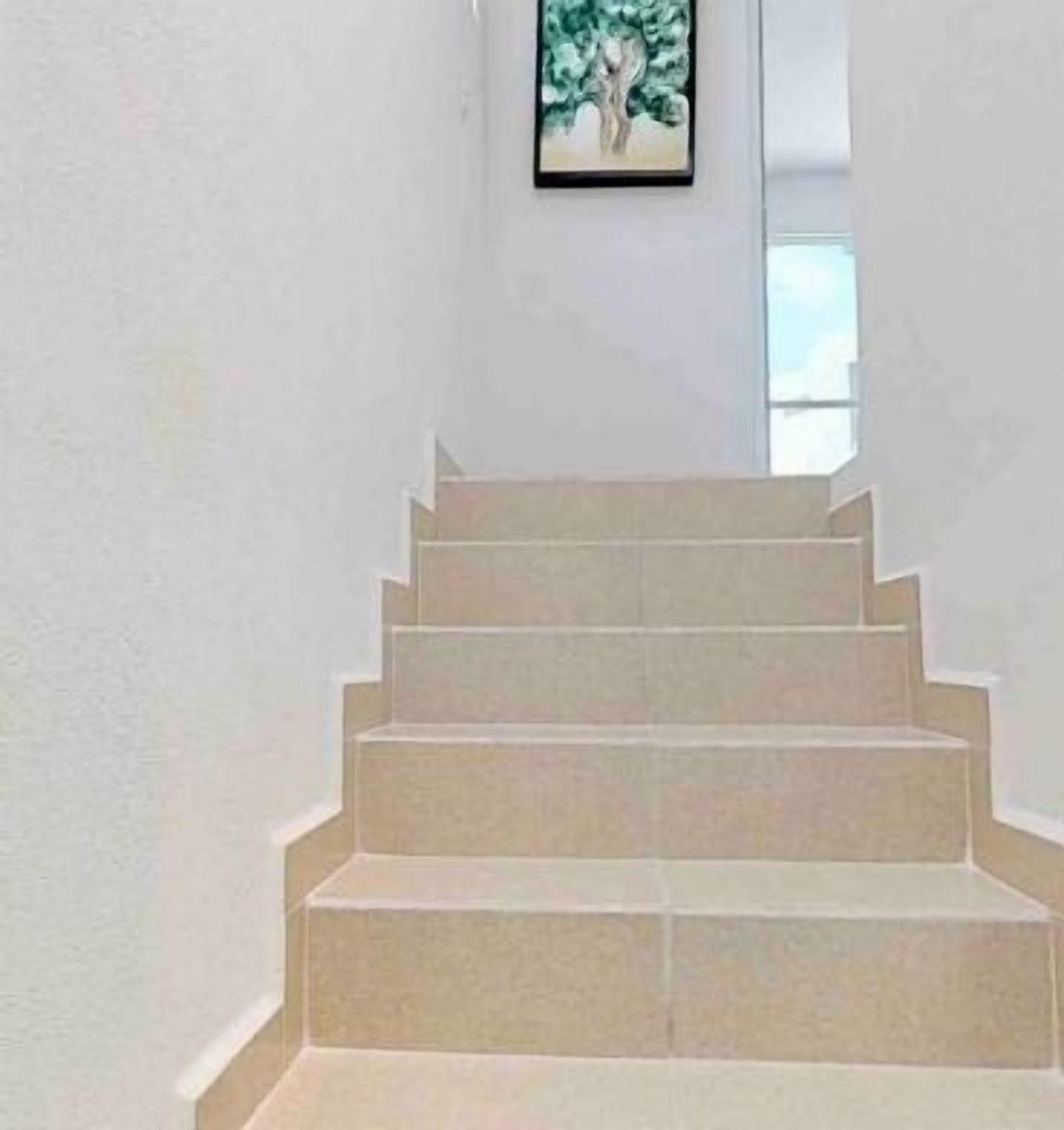 A staircase with a handrail, leading to a landing with a framed picture.
