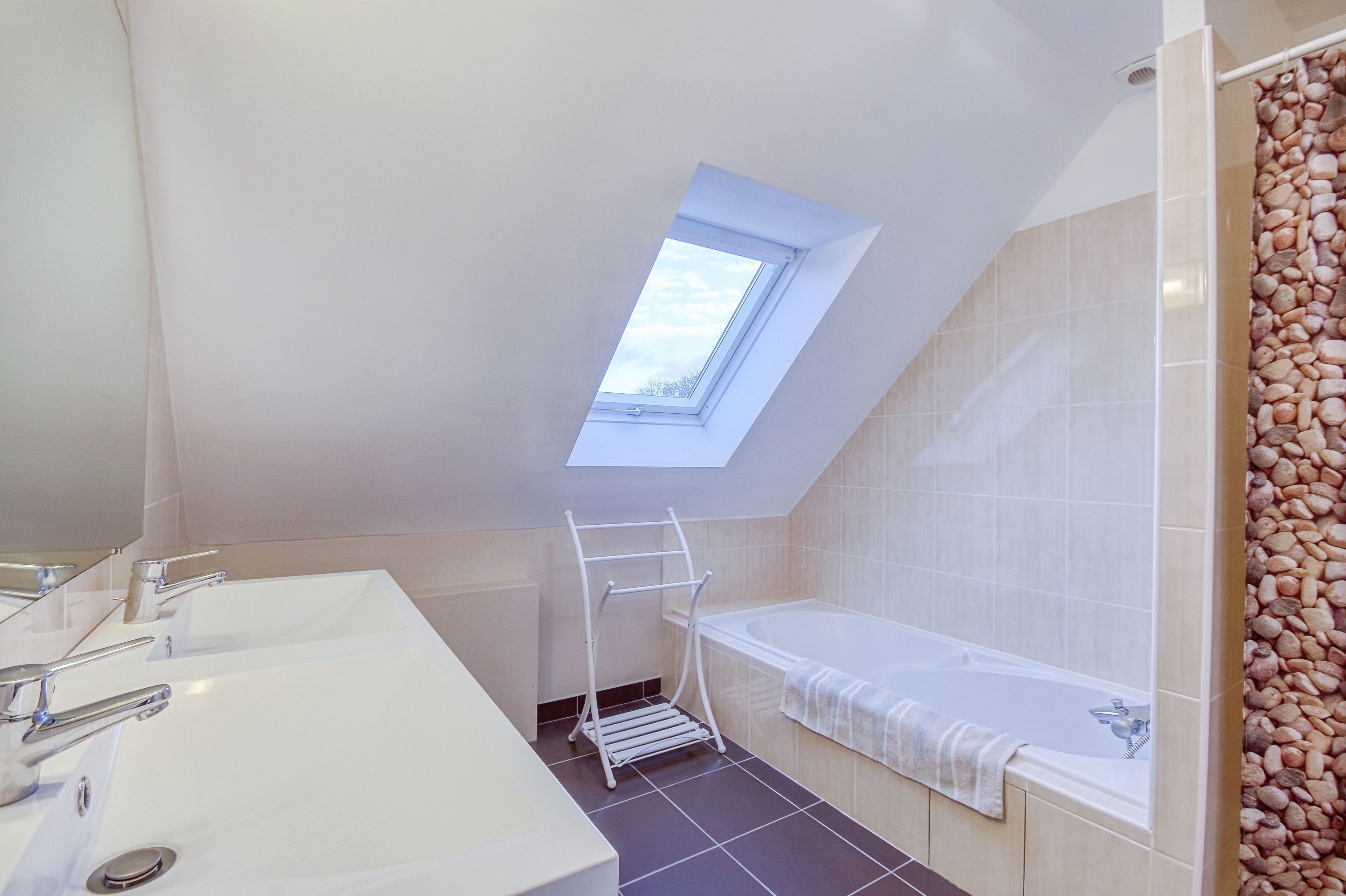 A modern bathroom with a skylight, a bathtub, and a white sink with a towel rack.
