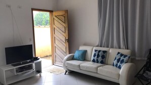 Ein Wohnzimmer mit einem weißen Sofa, einem Fernseher auf einem weißen Schrank und einer Tür, die nach draußen führt.