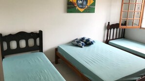 Ein Zimmer mit zwei Einzelbetten, einem hölzernen Kopfteil, einem Fenster mit Holzrahmen und einem Wandbild eines Schiffes vor Grün.