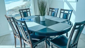 A dining area with a round table, six chairs, and a potted plant.