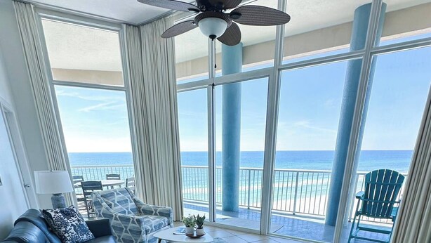 A spacious living room with a large blue sofa, a coffee table, and a view of the ocean through large windows.