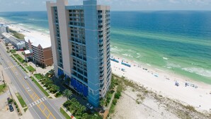 A high-rise hotel with multiple floors, a beach view, and a parking area with a road leading to the beach.