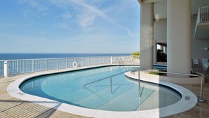 A pool with a view of the ocean, surrounded by a white railing and columns.