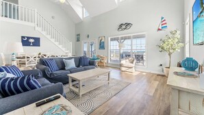 A spacious living room with a high ceiling, a staircase, and large windows.
