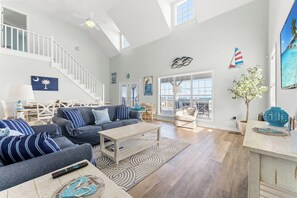 Un salon spacieux avec un haut plafond, un escalier et de grandes fenêtres.