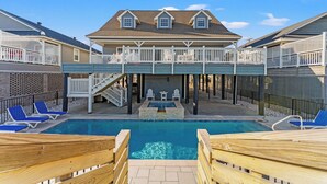 A pool area with a wooden deck, lounge chairs, and a covered seating area.