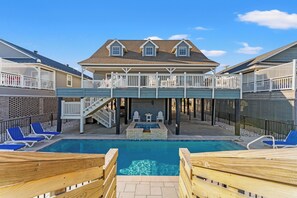 Un espace piscine doté d’une terrasse en bois, de chaises longues et d’un coin salon abrité.