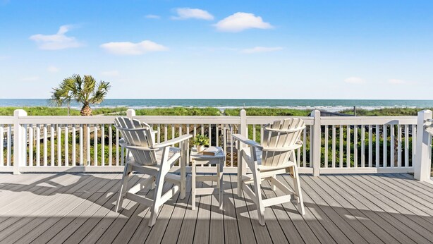 A wooden deck with white railings, two white chairs, and a small table.