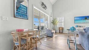 A spacious living room with a large window, wicker furniture, and a television.