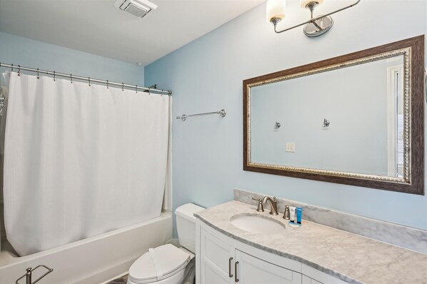 A bathroom with a bathtub, toilet, and sink with a mirror above. - Surfs Up, Beautiful 6 BR Ocean Front Home with Private Swimming Pool (North Myrtle Beach)