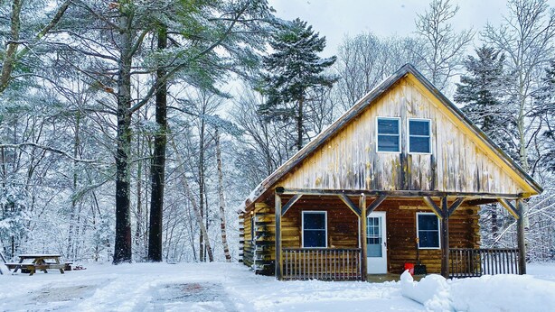 Een houten hut met een veranda, omringd door met sneeuw bedekte bomen.