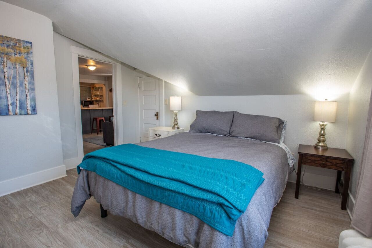 A bedroom with a large bed, two bedside tables with lamps, a door leading to a bathroom, and a painting on the wall.