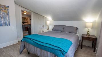 A bedroom with a large bed, two bedside tables with lamps, a door leading to a bathroom, and a painting on the wall.