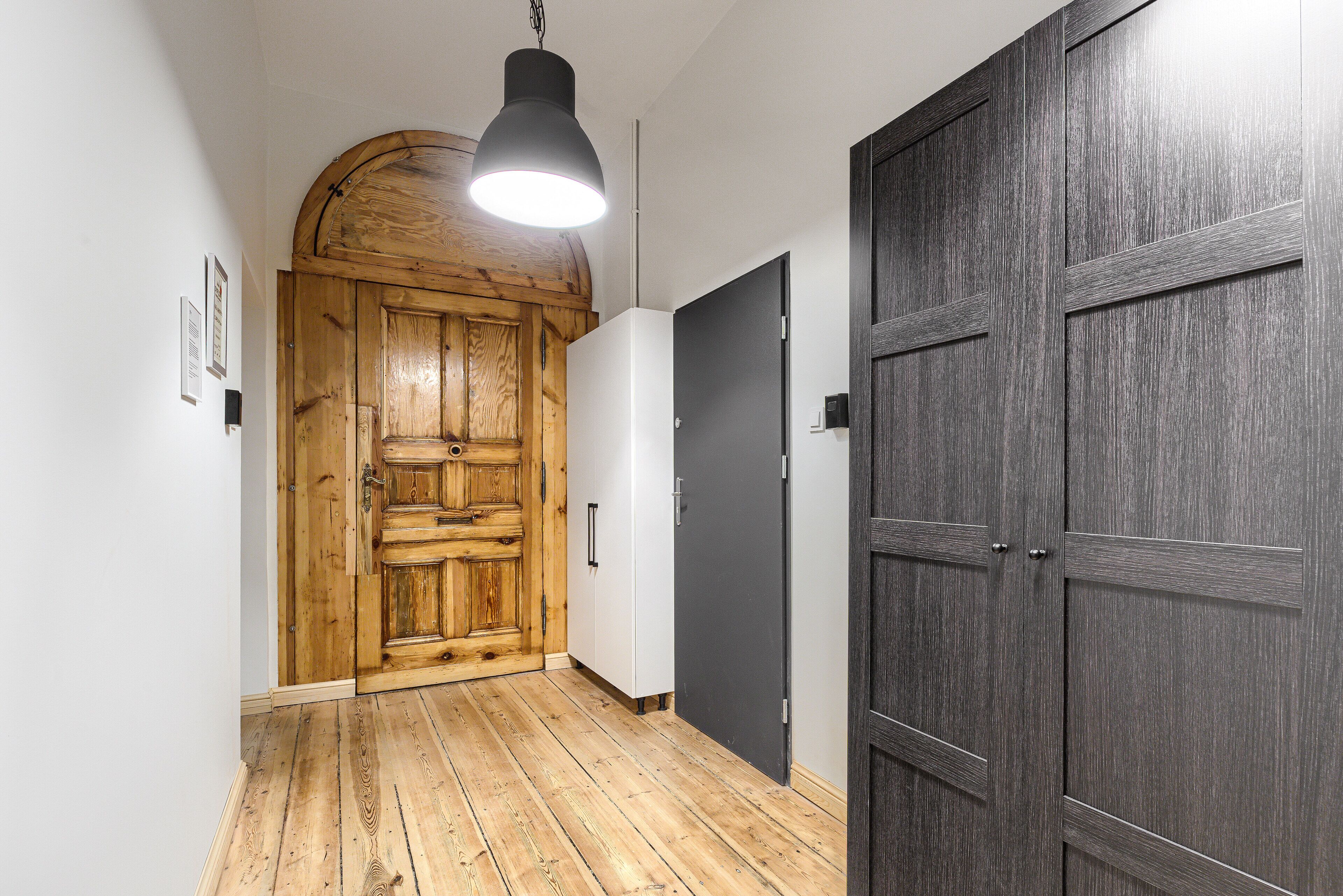 Un pasillo con suelo de madera, una puerta grande de madera y una puerta negra moderna.