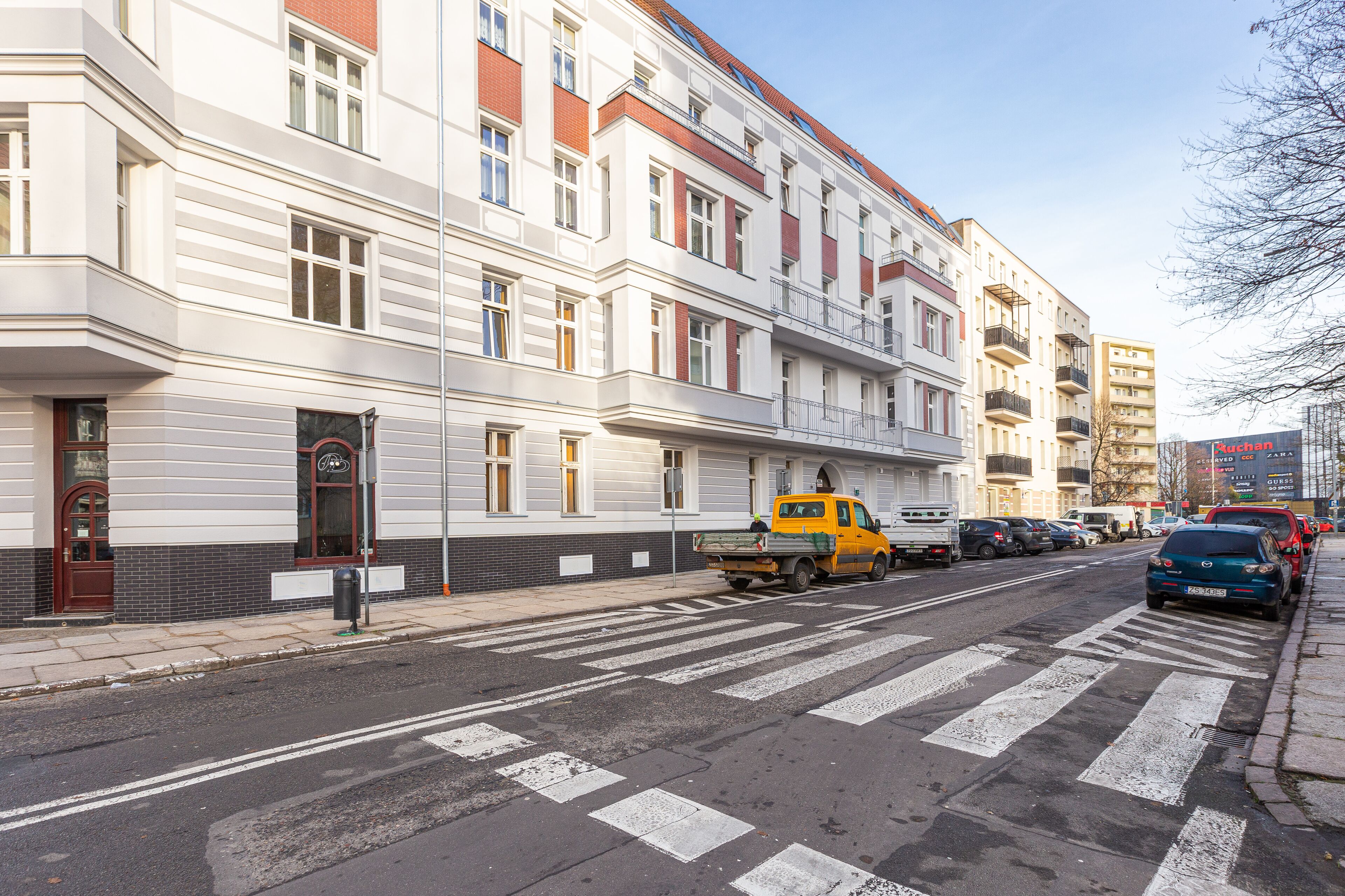 Una calle con un camión amarillo estacionado al costado, edificios con múltiples ventanas y balcones, y un cielo despejado.