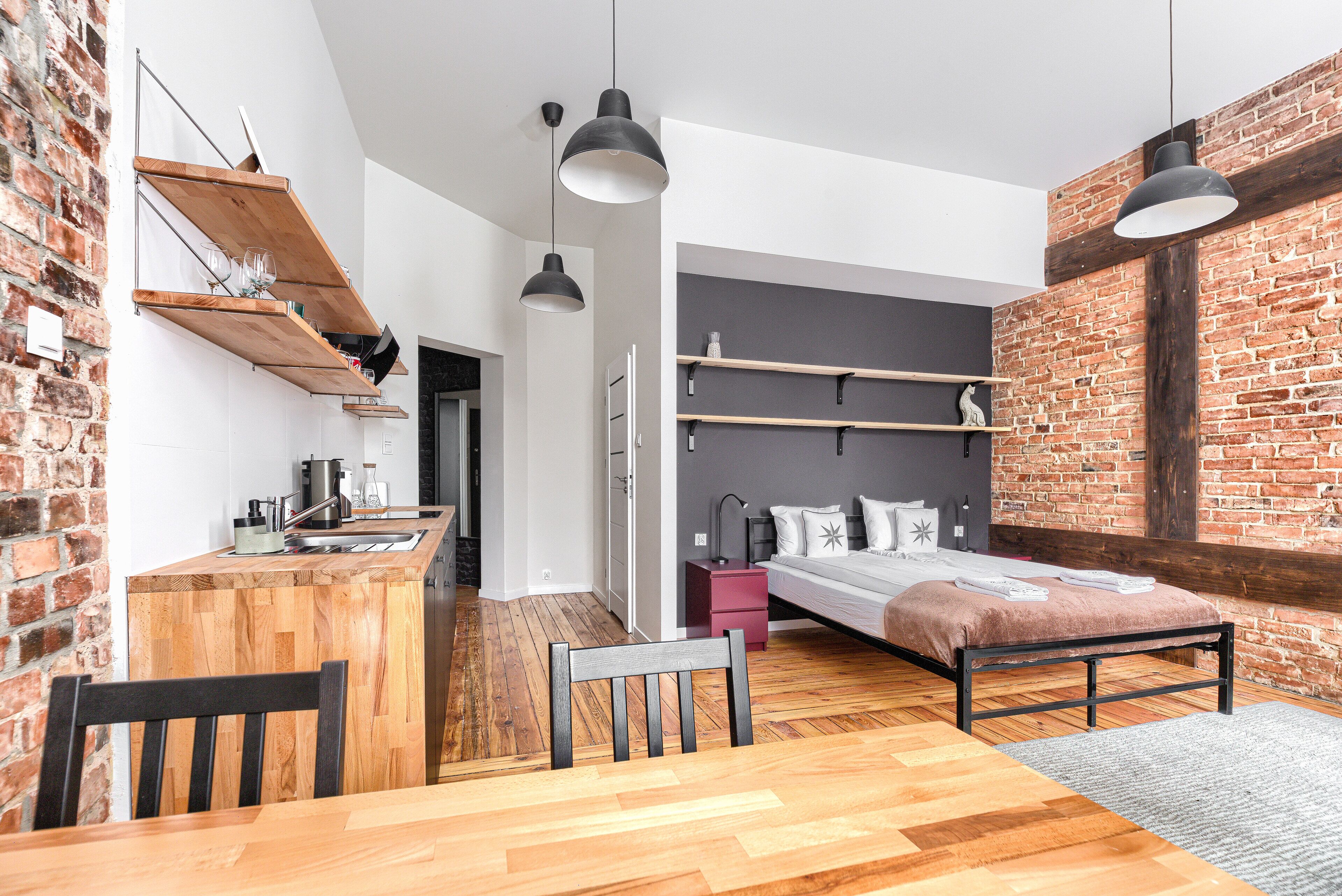 Habitació compacte i moderna amb zona de cuina, un llit amb capçal i una taula de menjador amb cadires.