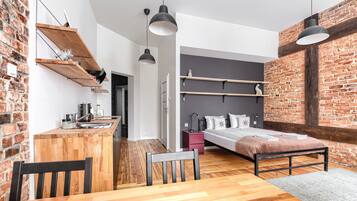 Habitació compacte i moderna amb zona de cuina, un llit amb capçal i una taula de menjador amb cadires.