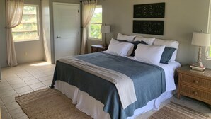 A bedroom with a bed, nightstands, a ceiling fan, and a large window with curtains. - Breezy Hilltop, Hart Bay View, only minutes from town (Cruz Bay)