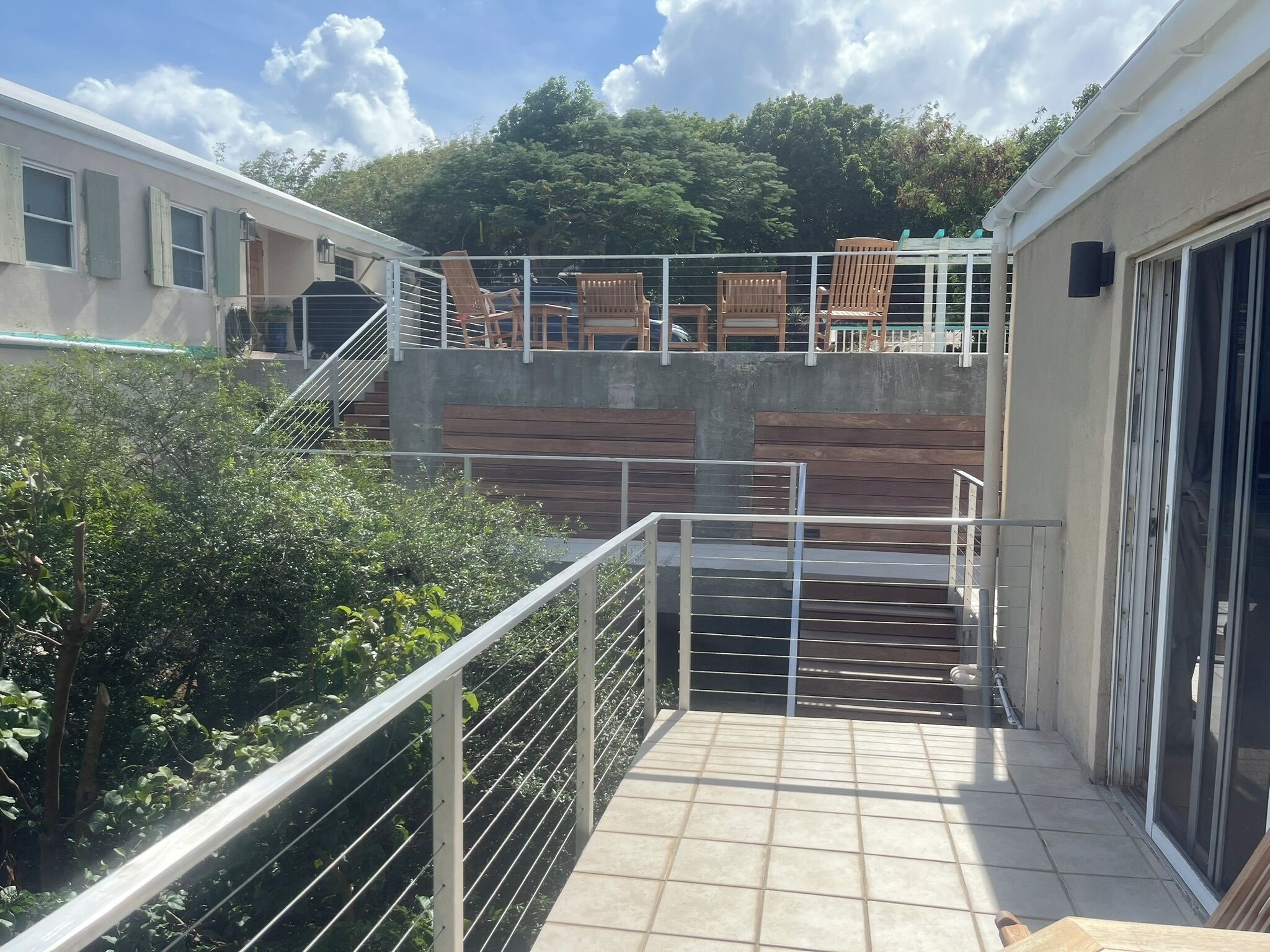 A balcony with a tiled floor, metal railing, and wooden chairs.