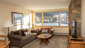 A cozy living room with a large window, a stone fireplace, a flat-screen TV, and a wooden coffee table. - On Keystone Lake/Shuttle to Lifts/Pool and Hot Tub Access/Great Amenities (dillon)