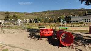 A playground with a metal climbing structure, red cylindrical play equipment, and a green slide. - On Keystone Lake/Shuttle to Lifts/Pool and Hot Tub Access/Great Amenities (dillon)