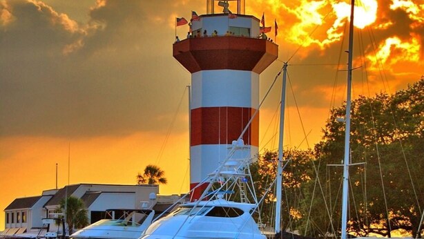 A lighthouse with a red and white striped tower, surrounded by boats and yachts docked at a marina. - 3 Bdrm Waterfront Villa in Harbour Town- Relax to the sounds of the Calibogue (Hilton Head Island)