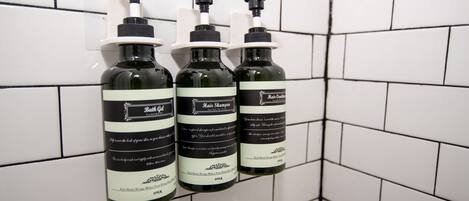 Three bottles of bath oil and hair shampoo on a tiled wall.