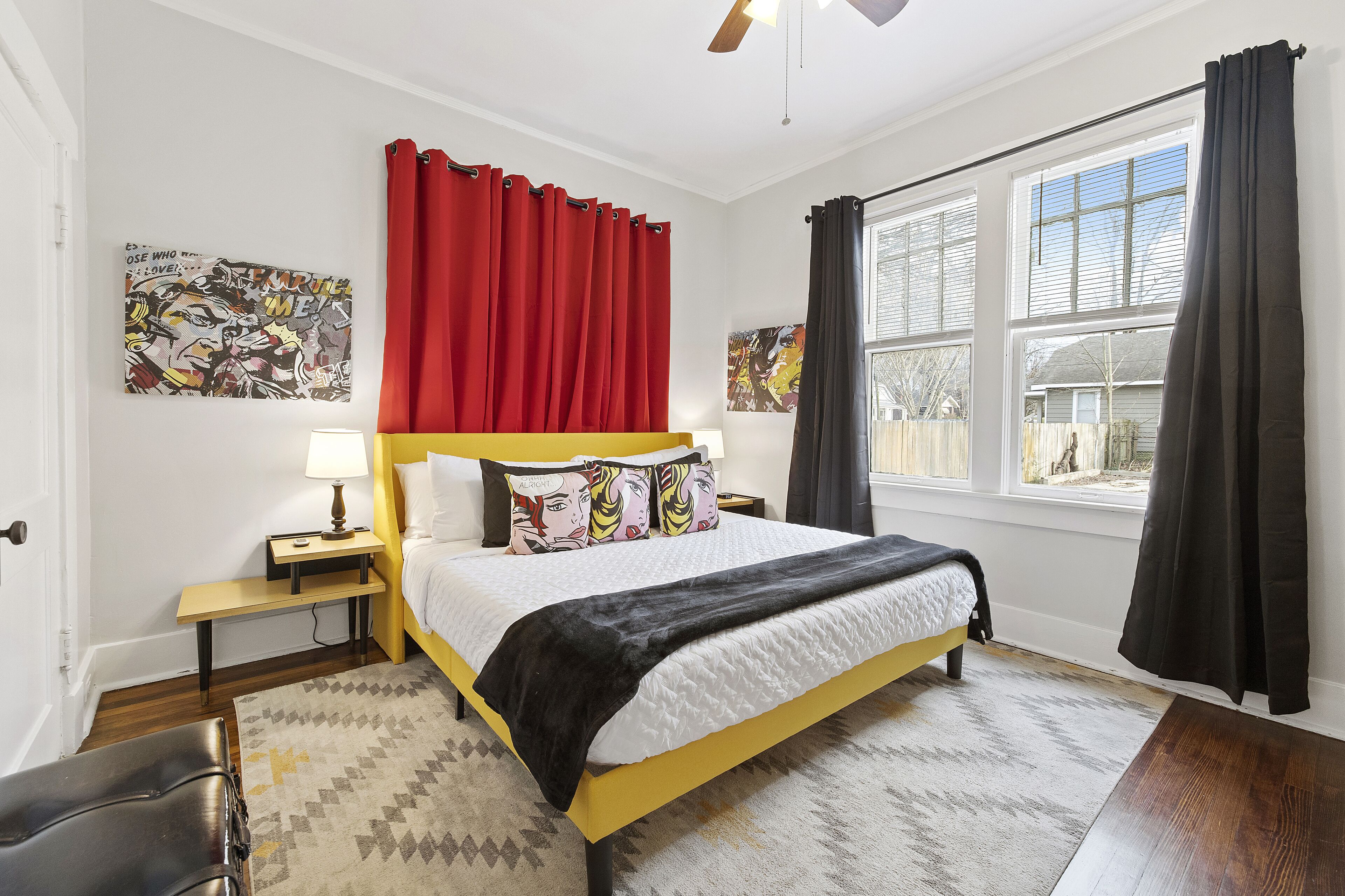 Un dormitorio con cama, mesitas de noche, un banco y una ventana con cortinas.