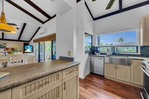 A modern kitchen with wooden cabinets, a granite countertop, and a large window offering a view of the outdoors.