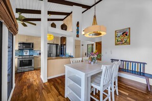 A spacious kitchen with modern appliances, a dining area with white furniture, and a wooden floor.